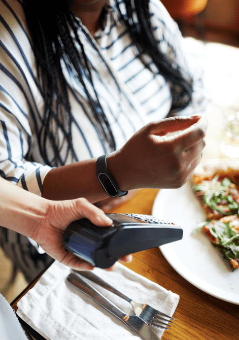 Woman holding hand with smartwatch close to payment machine held by waiter