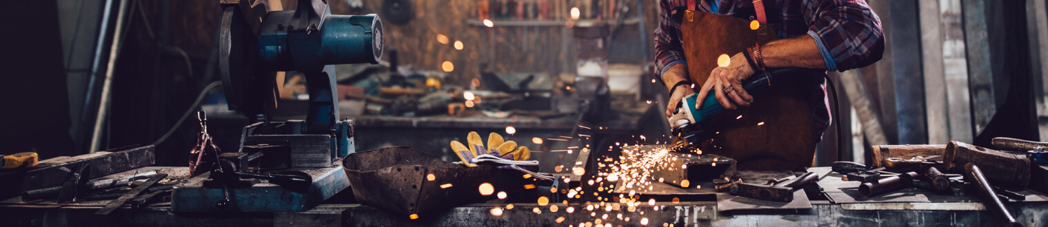 Man in a workshop holding a power tool up to metal causing sparks to fly