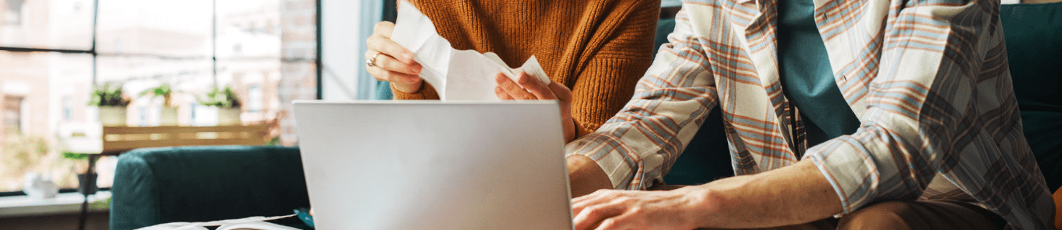 Two business owners sitting Infront of a laptop reviewing checks and invoices.