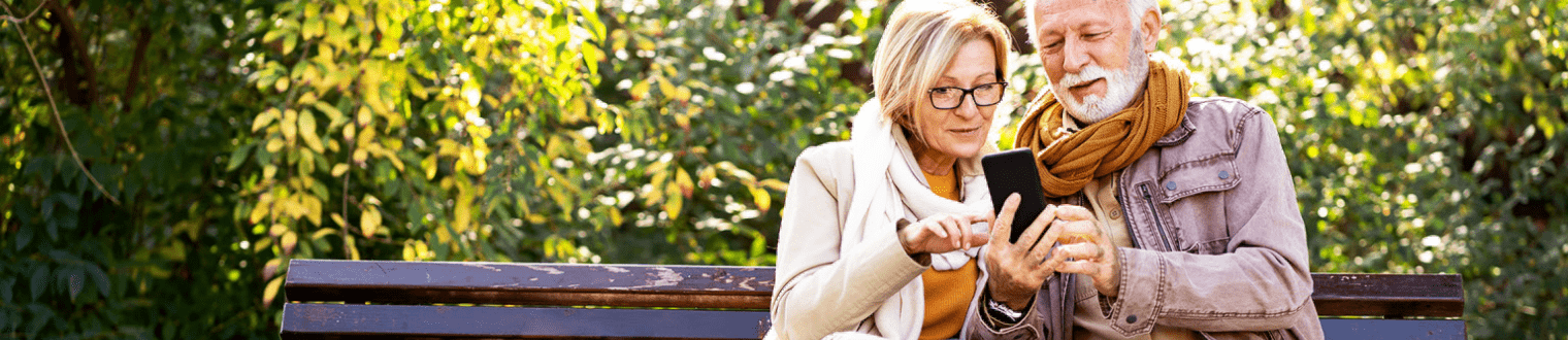 Cheerful elderly couple using banking apps on a smartphone to make payments outdoors in the park