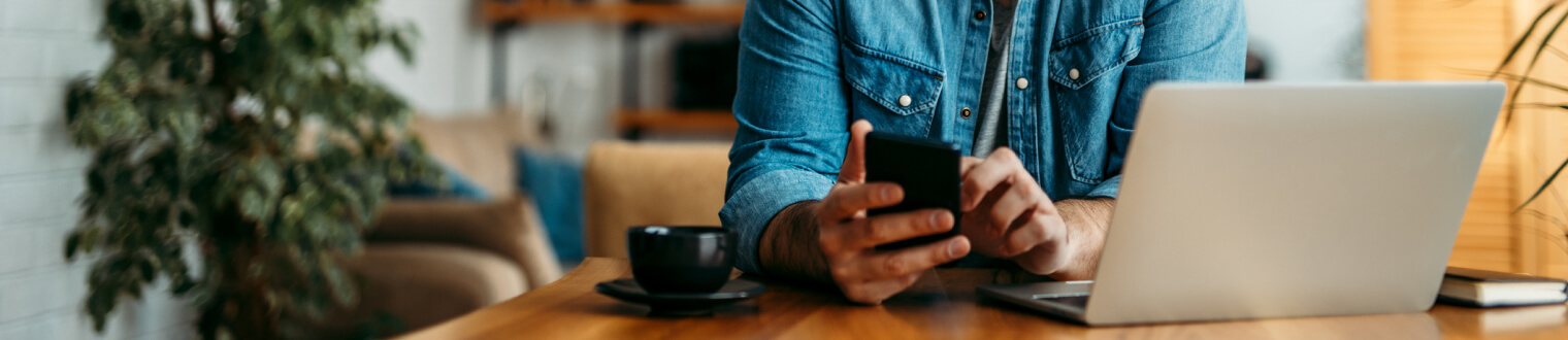 Man in an office holding a smartphone and looking at a laptop