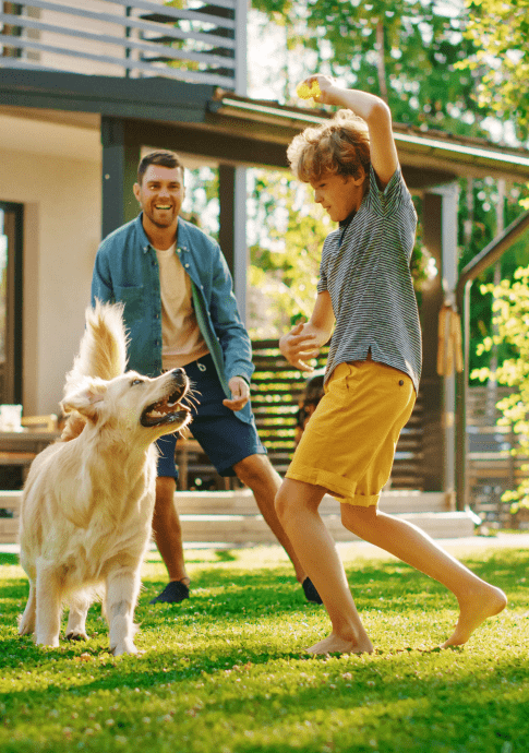 Father and son outside house playing ball with dog