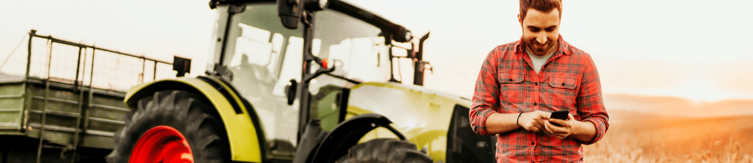 Male farmer working in field using smartphone in front of tractor.