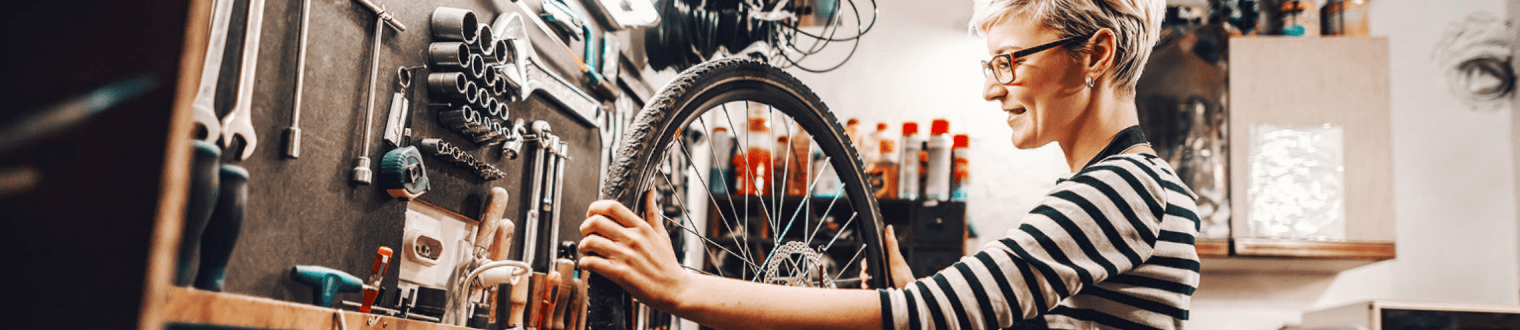 female worker holding and repairing bicycle wheel while standing in bicycle workshop.