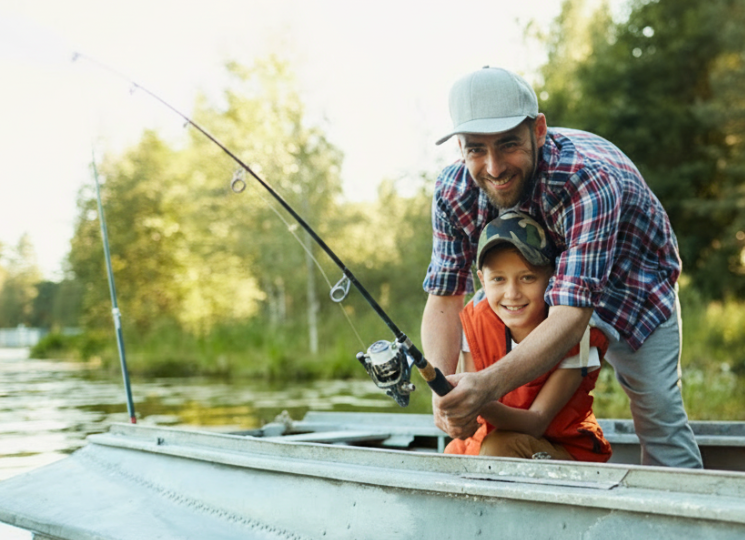 Happy father and son holding rod while sitting in boat and fishing in natural environment