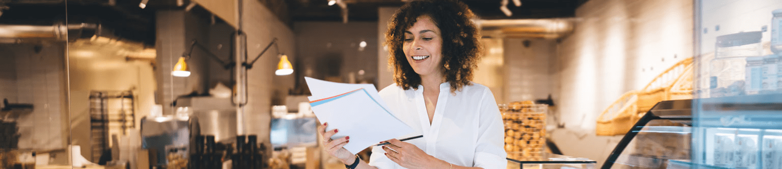 Woman business owner in baker analyzing paper documents for order delivery.